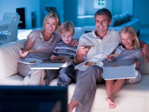 Family eating pizza and watching TV on sofa